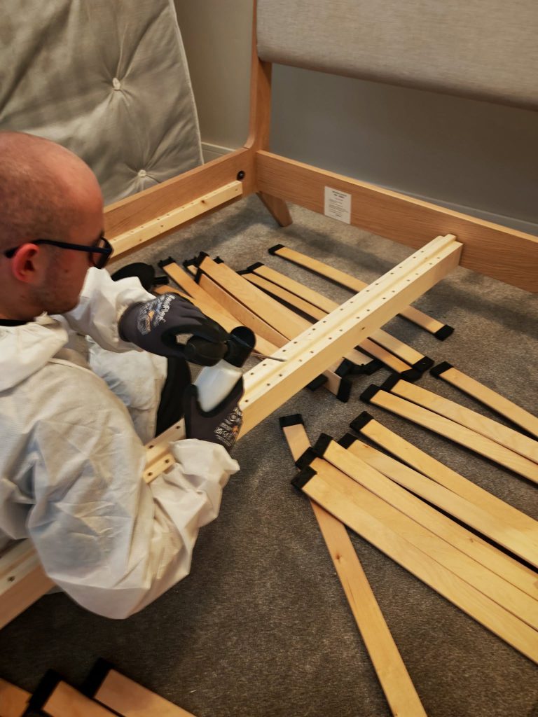 Man in protective clothing applying bed bug treatment to wooden bedframe